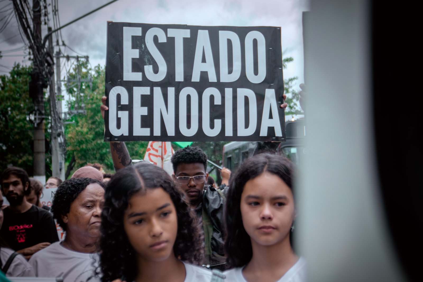 Manifestantes na Estrada de Itaquera, rumo ao Hospital Campo Limpo em destaque jovem com cartaz 'Estado Genocída'