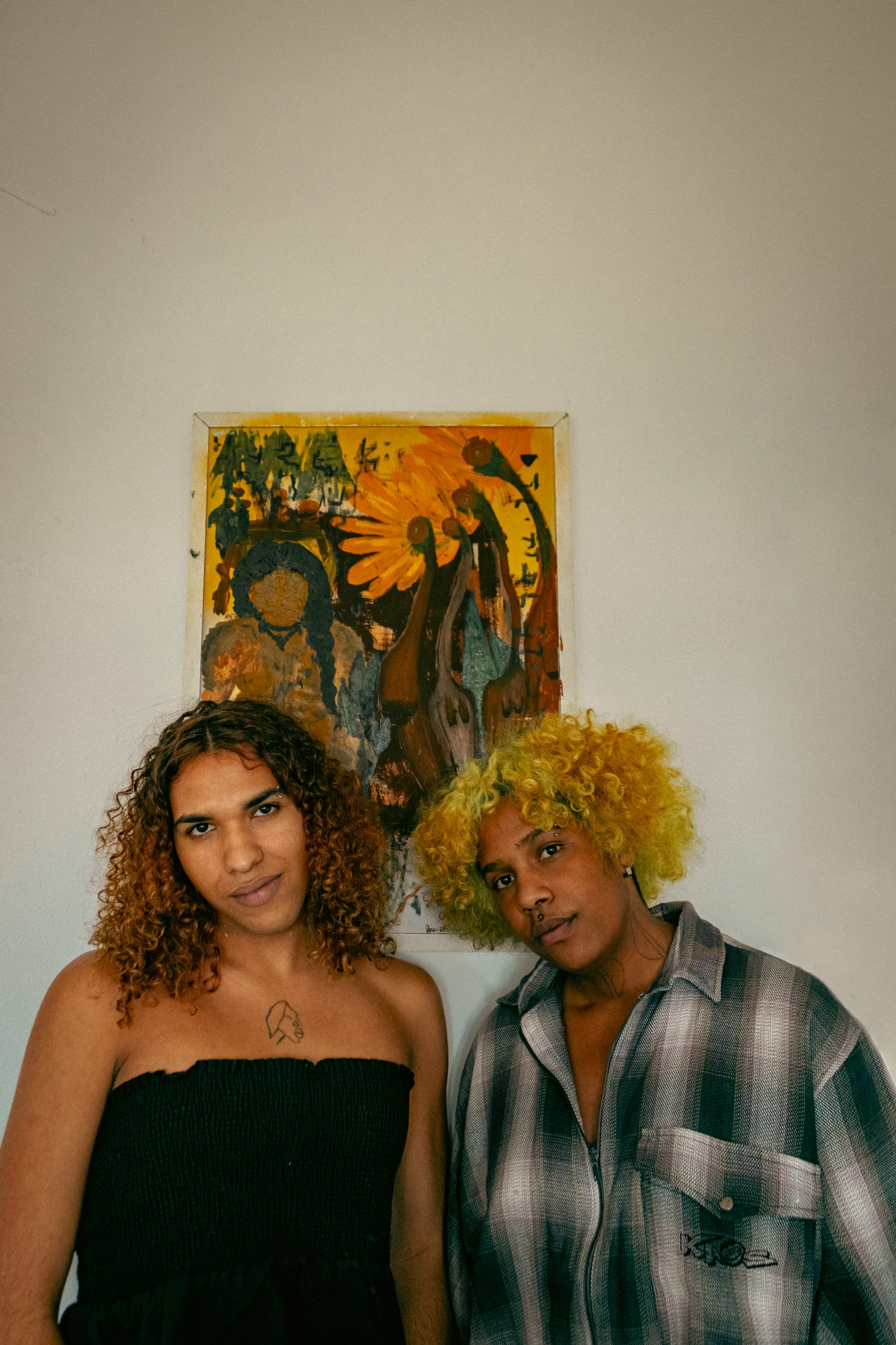 Edlene Sousa (ela/dela), à esquerda da foto, e Zure Rodrigues (ele/dele), à direita, posando com uma das telas que produziram em conjunto.