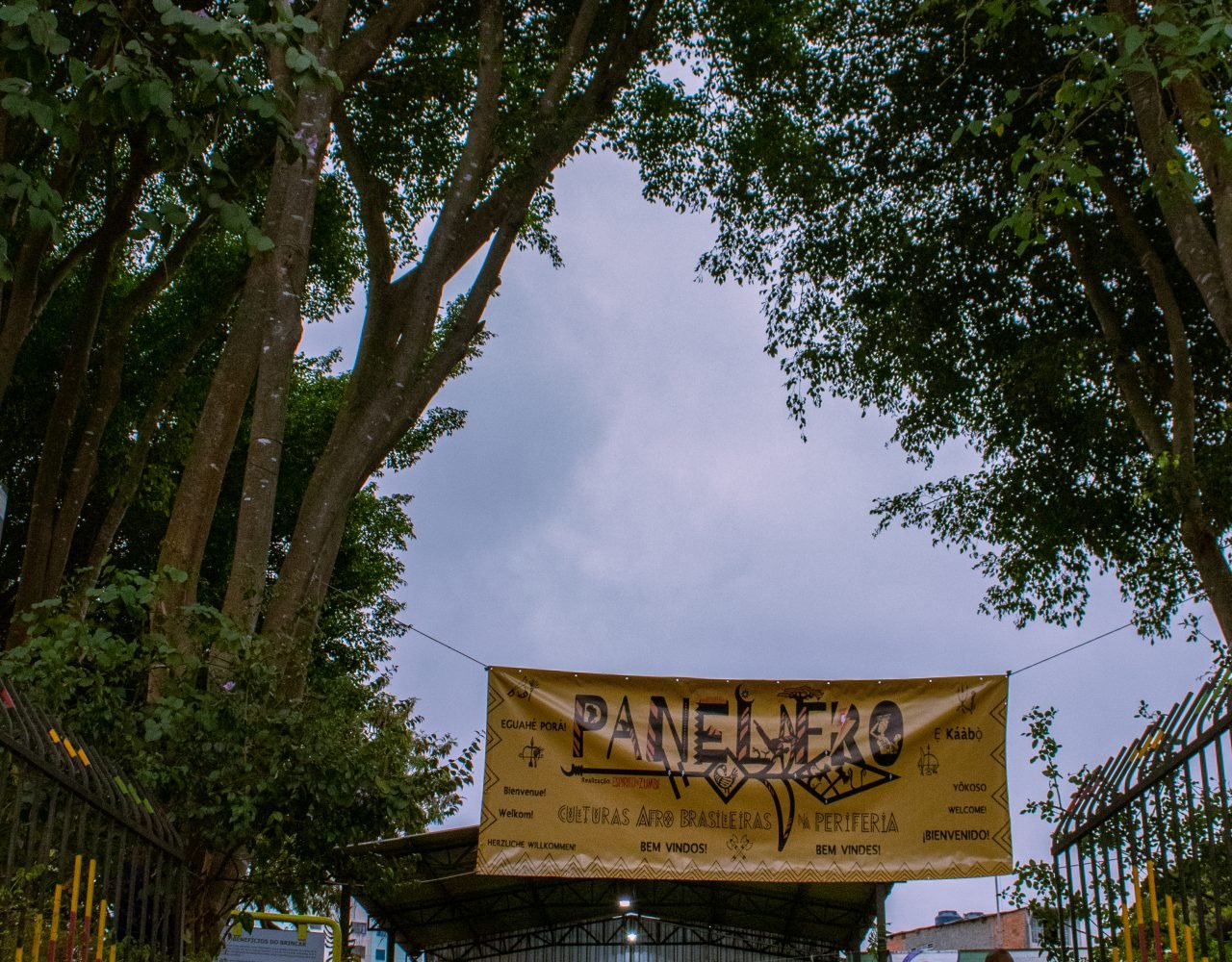 Entrada da Casa de Cultura M'Boi Mirim com faixa do Panelafro entre as árvores. - PANELAFRO_evento_culturapopular_zona sul_vitorijumapili-2