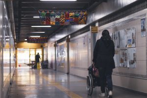 No corredor da escola, uma pessoa conduz uma criança cadeirante. A escola é acessível