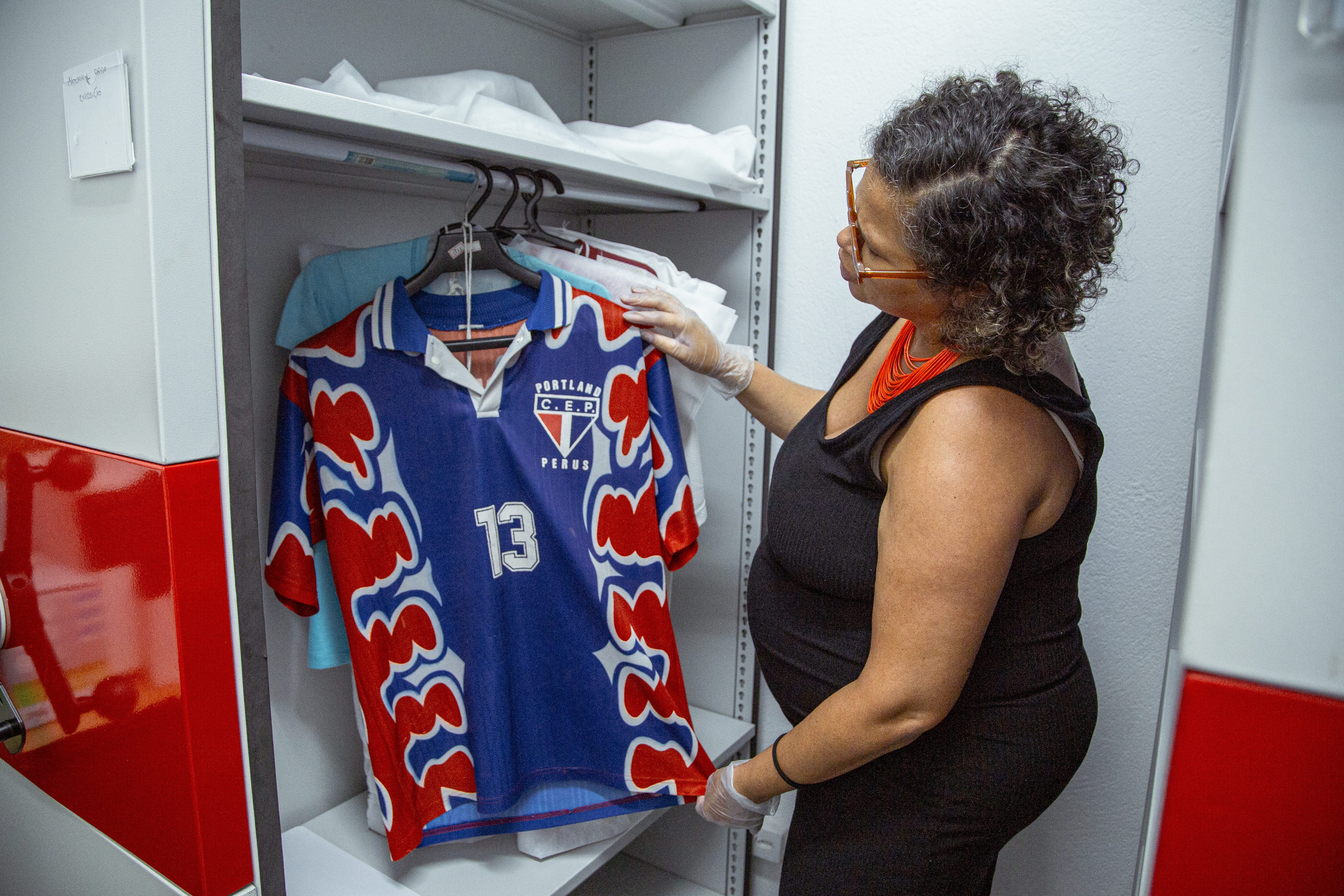 Sheila Moreira manuseia coleção de camisas do acervo. Dentre elas, do clube de mães do bairro e do time da região na época da fábrica